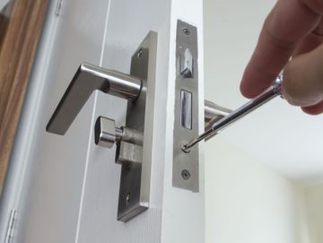 Vitt öppen dörr med silverfärgat handtag där man kan se en hand som skruvar dit låset