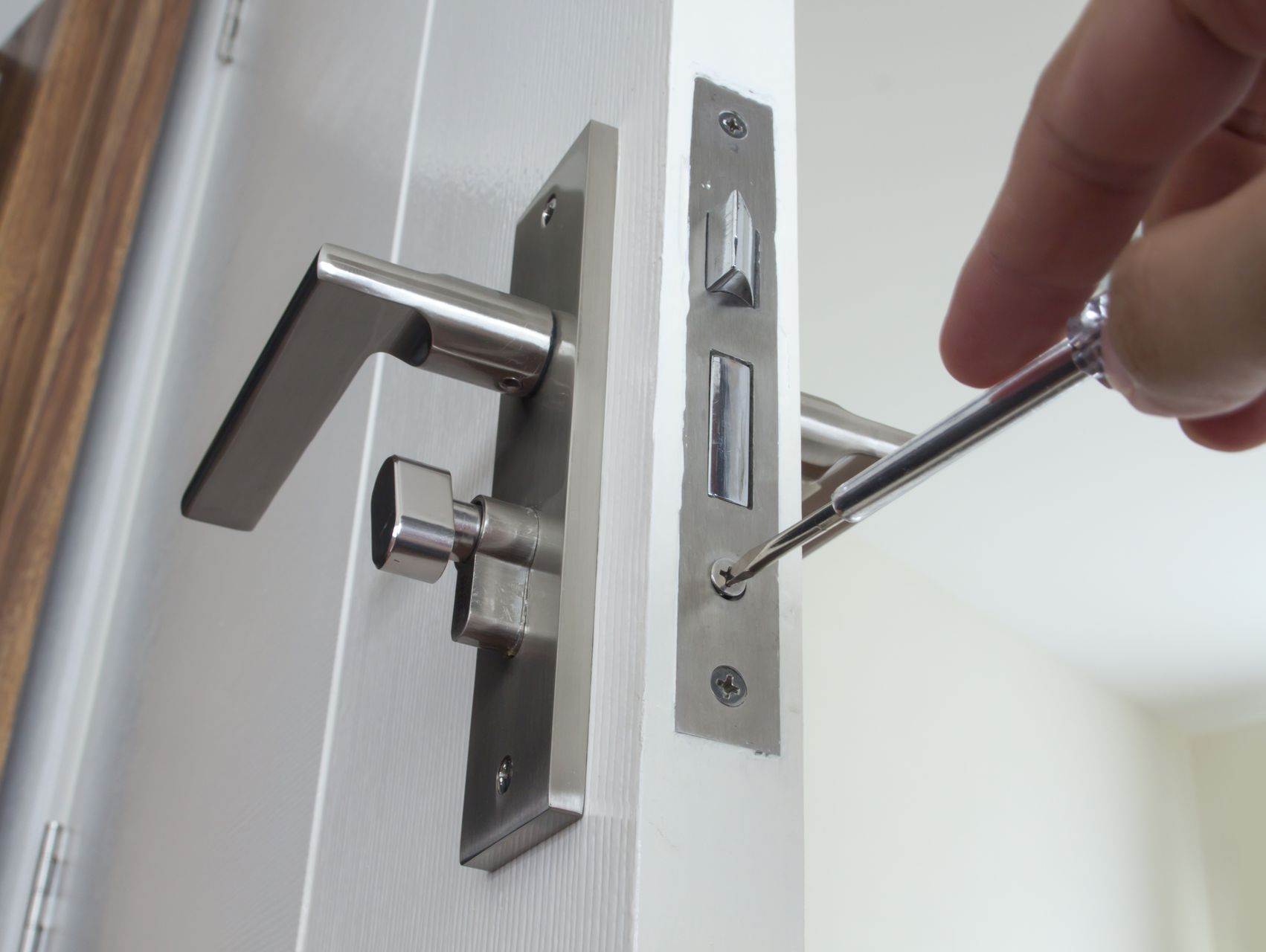 Vitt öppen dörr med silverfärgat handtag där man kan se en hand som skruvar dit låset